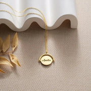 14k gold-filled necklace with a round pendant engraved with 'Amelia' on a textured surface with leaves.